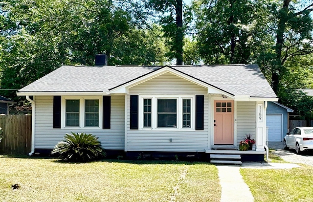 view of front of property featuring a garage, a shingled roof, a front lawn, and fence