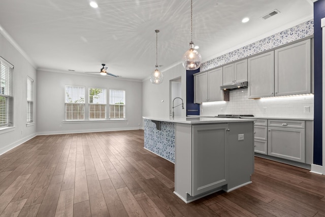 kitchen featuring gray cabinetry, ornamental molding, light countertops, a ceiling fan, and a kitchen island with sink