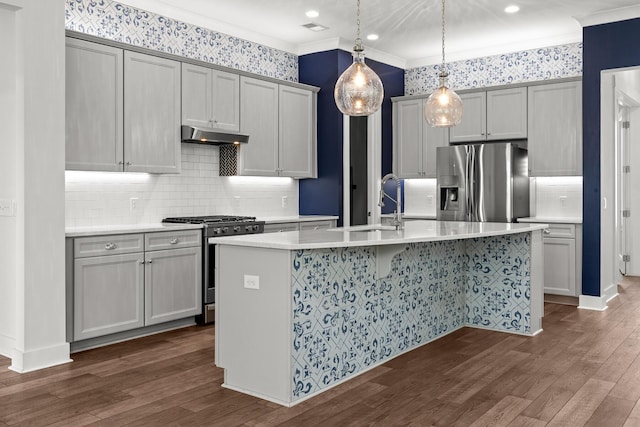 kitchen with stainless steel appliances, dark wood finished floors, an island with sink, decorative backsplash, and light countertops