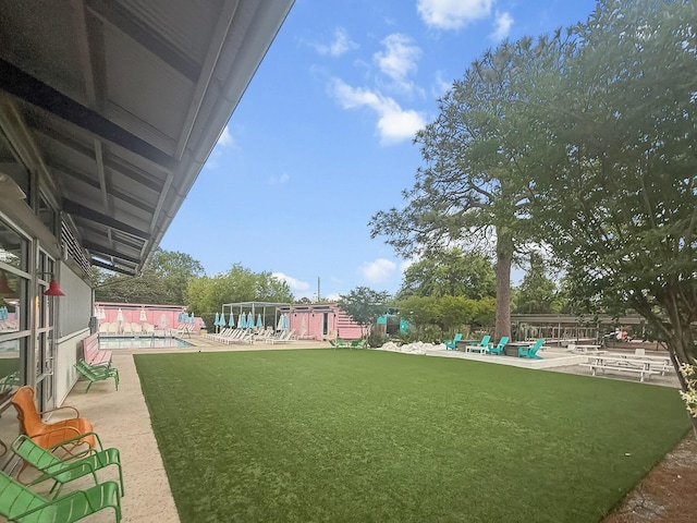 view of grassy yard with a community pool and a patio area