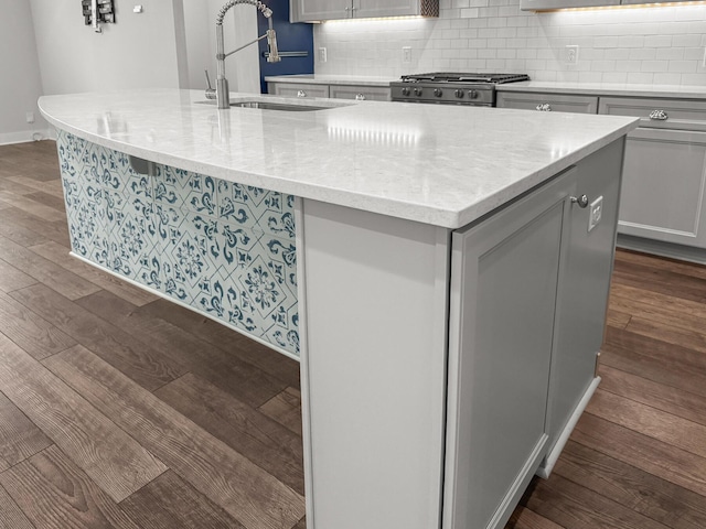 kitchen with a sink, dark wood finished floors, decorative backsplash, range, and a center island with sink