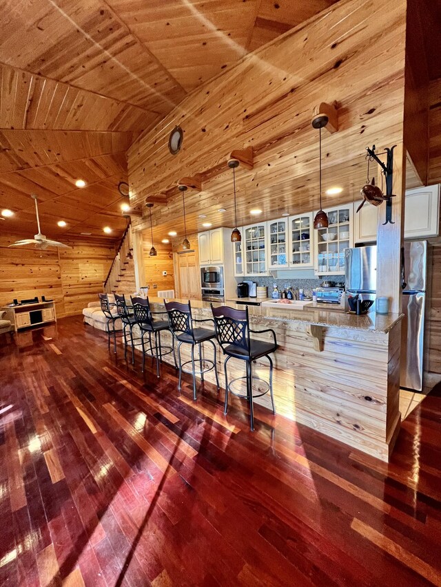 interior space with ceiling fan, vaulted ceiling, wood-type flooring, wood walls, and wooden ceiling