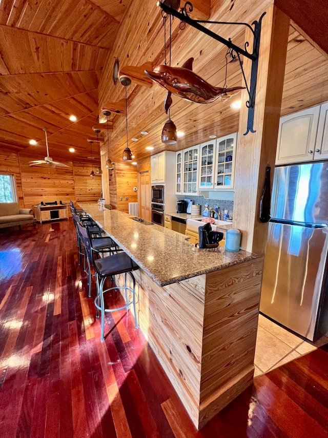 kitchen featuring light wood-type flooring, wood ceiling, a breakfast bar area, white cabinetry, and appliances with stainless steel finishes