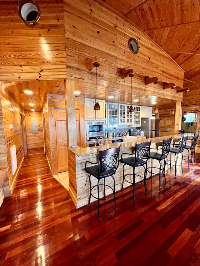 kitchen featuring appliances with stainless steel finishes, light wood-type flooring, wooden walls, a breakfast bar, and wooden ceiling