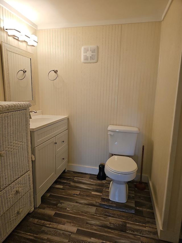 half bath with toilet, wood finished floors, vanity, and baseboards