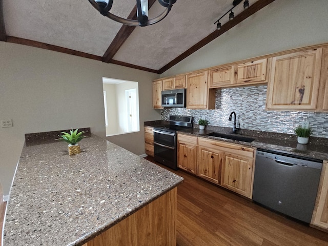 kitchen featuring stainless steel appliances, dark stone counters, vaulted ceiling, and a sink