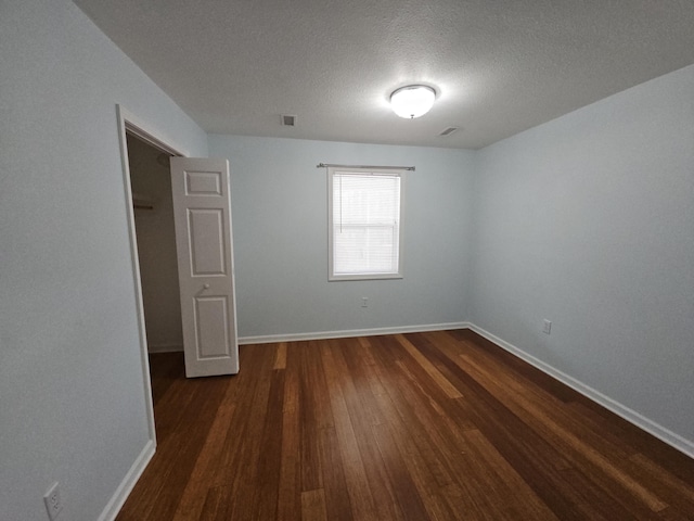 empty room with dark wood-style flooring, visible vents, a textured ceiling, and baseboards