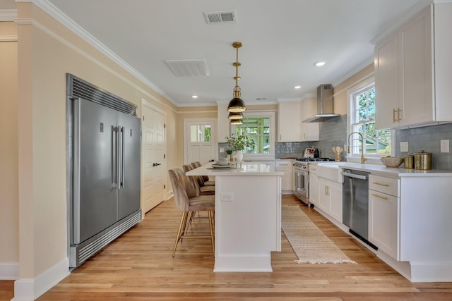 kitchen with wall chimney exhaust hood, pendant lighting, high quality appliances, white cabinets, and a center island