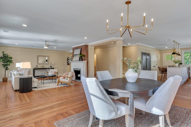 dining room featuring crown molding, a fireplace, light hardwood / wood-style floors, and ceiling fan with notable chandelier