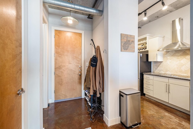 interior space featuring tasteful backsplash, freestanding refrigerator, white cabinets, concrete floors, and wall chimney exhaust hood