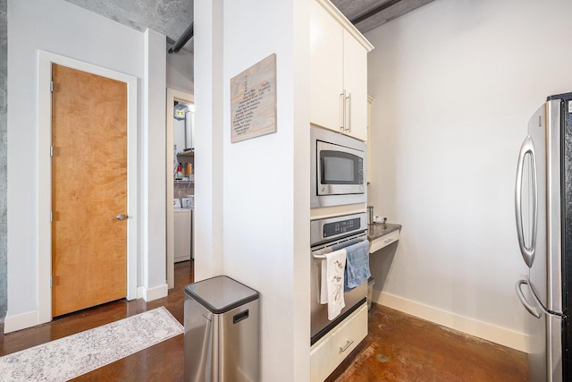 kitchen with finished concrete flooring, washer / dryer, baseboards, stainless steel appliances, and white cabinetry