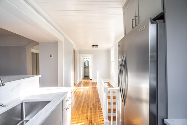 kitchen with gray cabinets, light stone counters, light hardwood / wood-style floors, sink, and stainless steel fridge