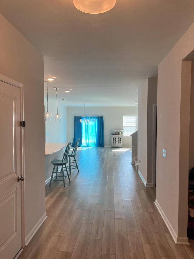 hall with wood finished floors, baseboards, and a chandelier