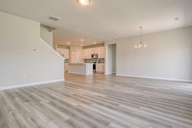 unfurnished living room with a chandelier, baseboards, light wood-style flooring, recessed lighting, and a sink