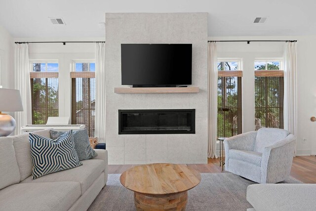 living area with a large fireplace, plenty of natural light, visible vents, and wood finished floors