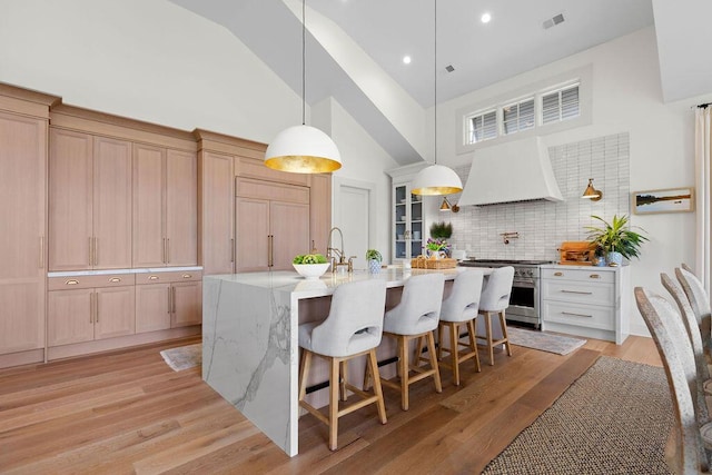 kitchen with high vaulted ceiling, visible vents, light wood finished floors, stainless steel stove, and custom range hood