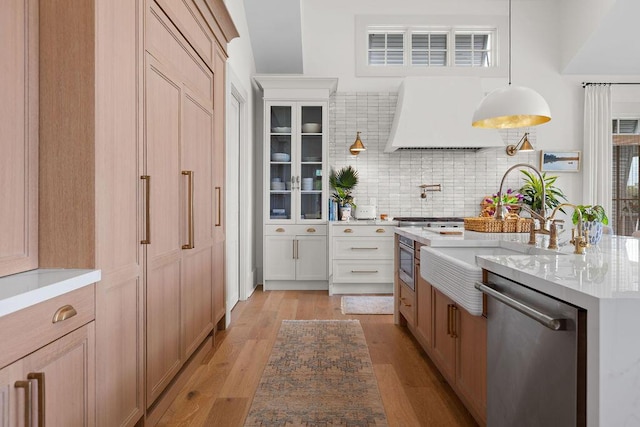 kitchen featuring light wood finished floors, stainless steel dishwasher, custom exhaust hood, and backsplash