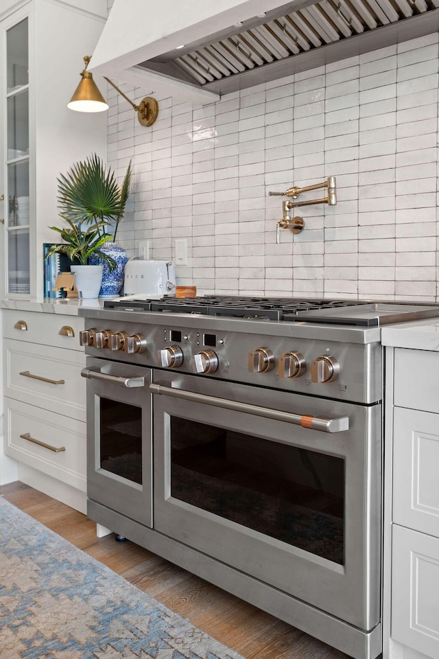 kitchen featuring range with two ovens, extractor fan, white cabinets, light wood-type flooring, and tasteful backsplash