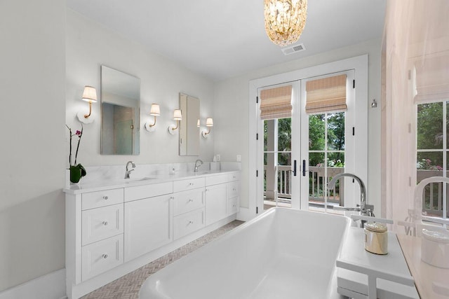bathroom featuring a sink, french doors, visible vents, a soaking tub, and a notable chandelier