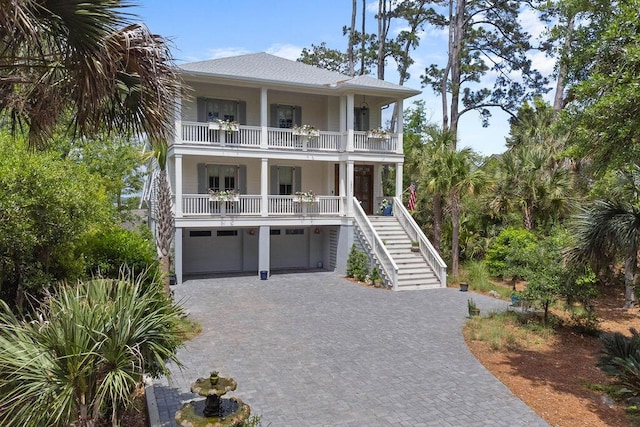 beach home featuring a balcony, decorative driveway, a porch, a garage, and stairway
