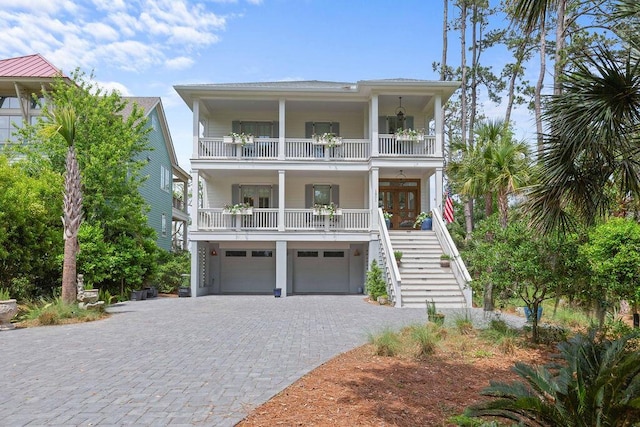 coastal home with an attached garage, decorative driveway, a balcony, a porch, and stairs