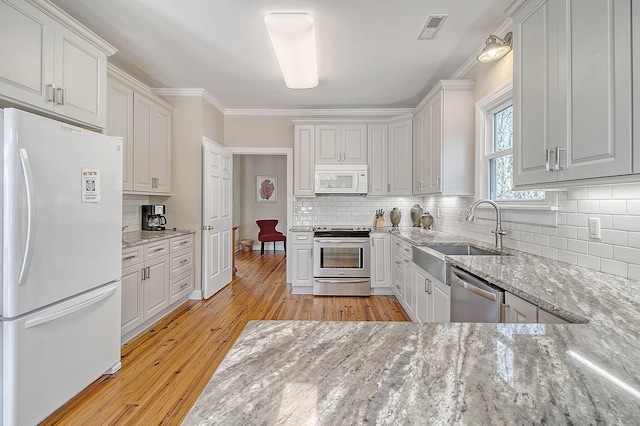 kitchen featuring sink, light hardwood / wood-style flooring, appliances with stainless steel finishes, light stone countertops, and white cabinets