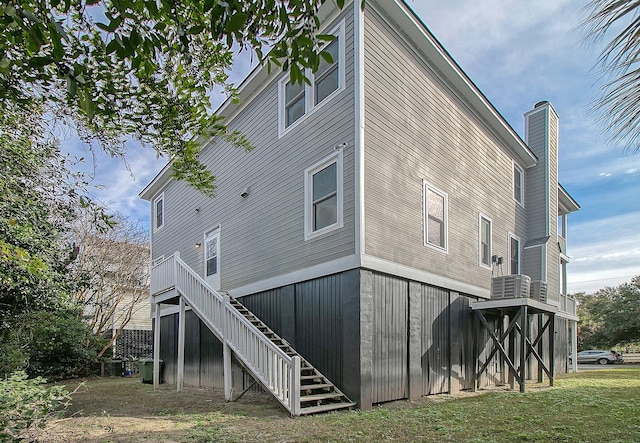 rear view of property with central AC unit and a lawn