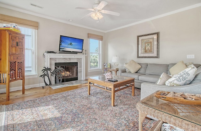 living room featuring hardwood / wood-style flooring, a premium fireplace, ceiling fan, and crown molding