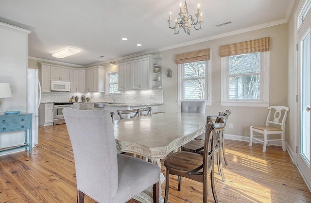 dining space with ornamental molding, sink, a chandelier, and light hardwood / wood-style floors