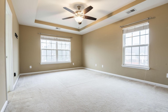 spare room featuring a tray ceiling, visible vents, carpet floors, and ceiling fan