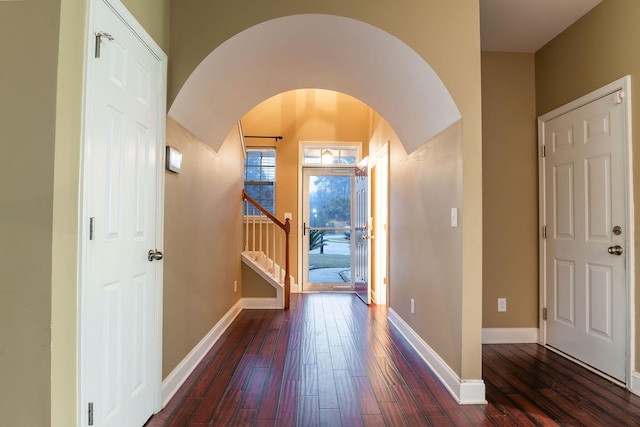 foyer entrance featuring baseboards, arched walkways, wood-type flooring, and stairs