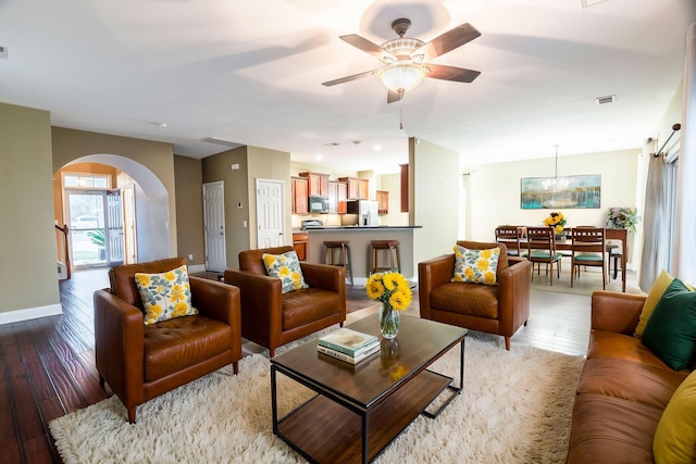 living area with visible vents, light wood finished floors, baseboards, arched walkways, and ceiling fan with notable chandelier