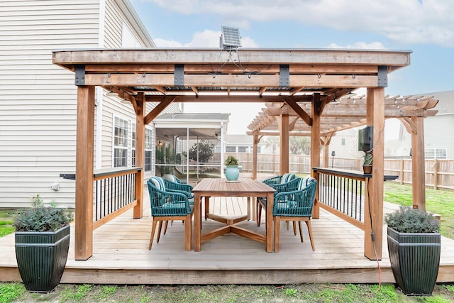 wooden deck featuring a sunroom, outdoor dining space, a pergola, and fence