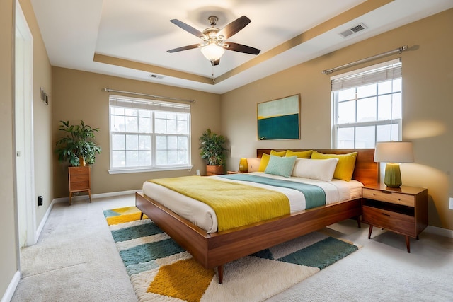 bedroom with visible vents, light colored carpet, baseboards, and a tray ceiling