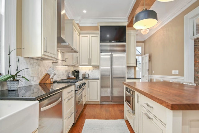 kitchen with wall chimney range hood, light hardwood / wood-style flooring, butcher block counters, high quality appliances, and ornamental molding