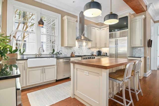 kitchen featuring a kitchen island, white cabinetry, sink, stainless steel appliances, and wall chimney range hood