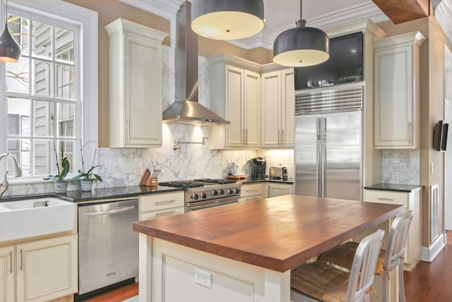 kitchen with sink, premium appliances, hanging light fixtures, crown molding, and wall chimney range hood