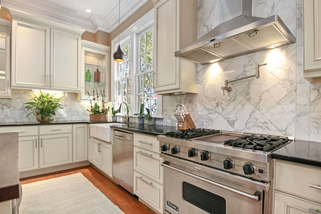 kitchen with wall chimney exhaust hood, sink, appliances with stainless steel finishes, ornamental molding, and backsplash