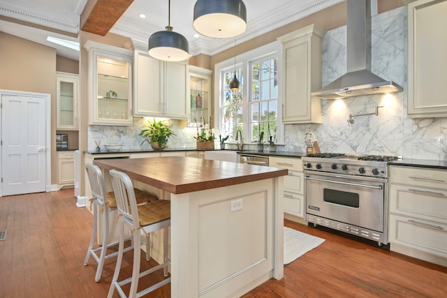 kitchen featuring pendant lighting, wall chimney range hood, wooden counters, appliances with stainless steel finishes, and a center island