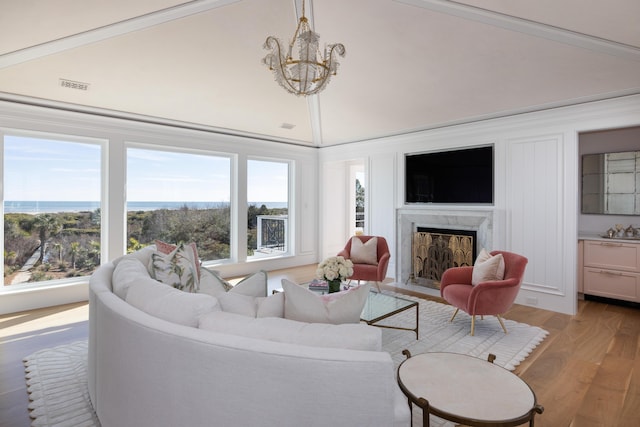 living room with a water view, wood-type flooring, a chandelier, high vaulted ceiling, and a fireplace