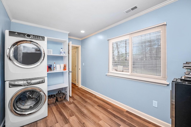 clothes washing area featuring stacked washer / drying machine, crown molding, wood finished floors, baseboards, and recessed lighting