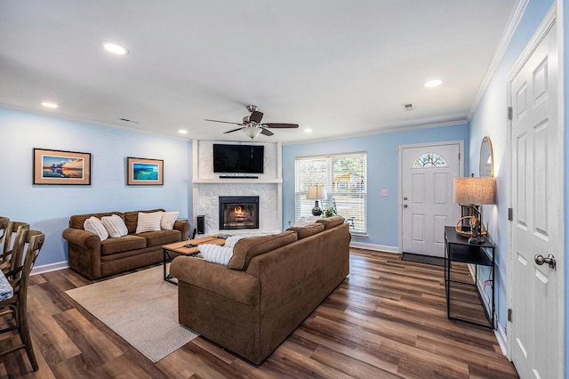 living area with crown molding, a ceiling fan, a stone fireplace, dark wood-type flooring, and baseboards