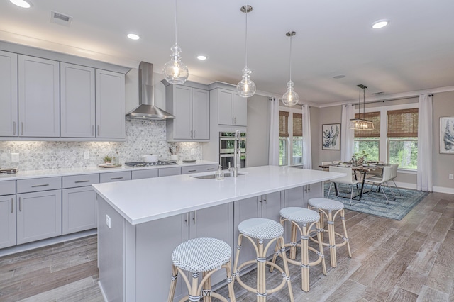 kitchen with wall chimney exhaust hood, pendant lighting, a kitchen bar, a center island with sink, and appliances with stainless steel finishes