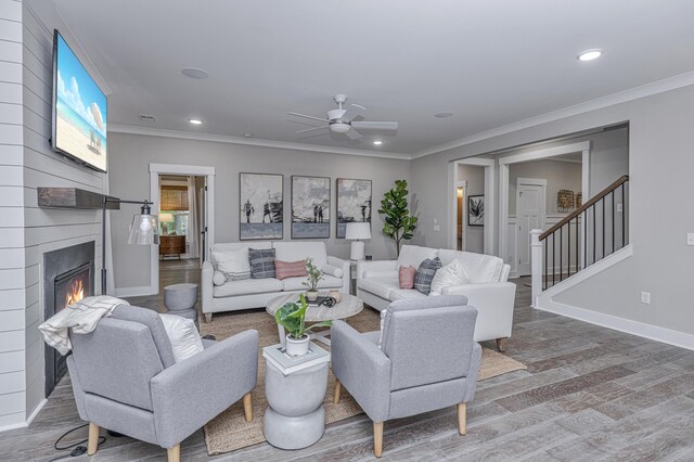 living room featuring ceiling fan, a large fireplace, wood-type flooring, and crown molding