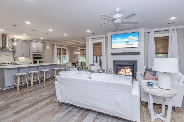 living room with ceiling fan, a large fireplace, and light hardwood / wood-style floors