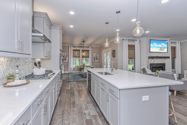 kitchen with a center island with sink, sink, light wood-type flooring, a fireplace, and decorative light fixtures