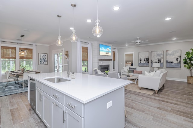 kitchen featuring stainless steel dishwasher, a large fireplace, a kitchen island with sink, ceiling fan, and pendant lighting