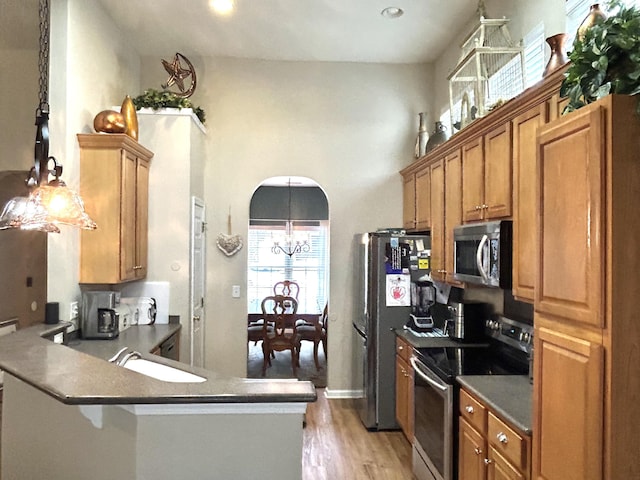 kitchen featuring arched walkways, brown cabinetry, dark countertops, appliances with stainless steel finishes, and a sink