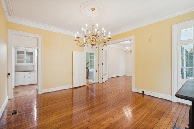 empty room featuring wood-type flooring, crown molding, and a chandelier