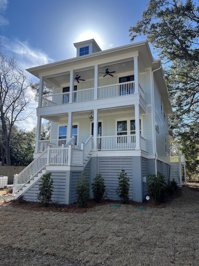 coastal home with a balcony, covered porch, ceiling fan, and stairs